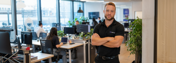 A tabnav team member standing in a modern open-plan office with colleagues working at desks in the background